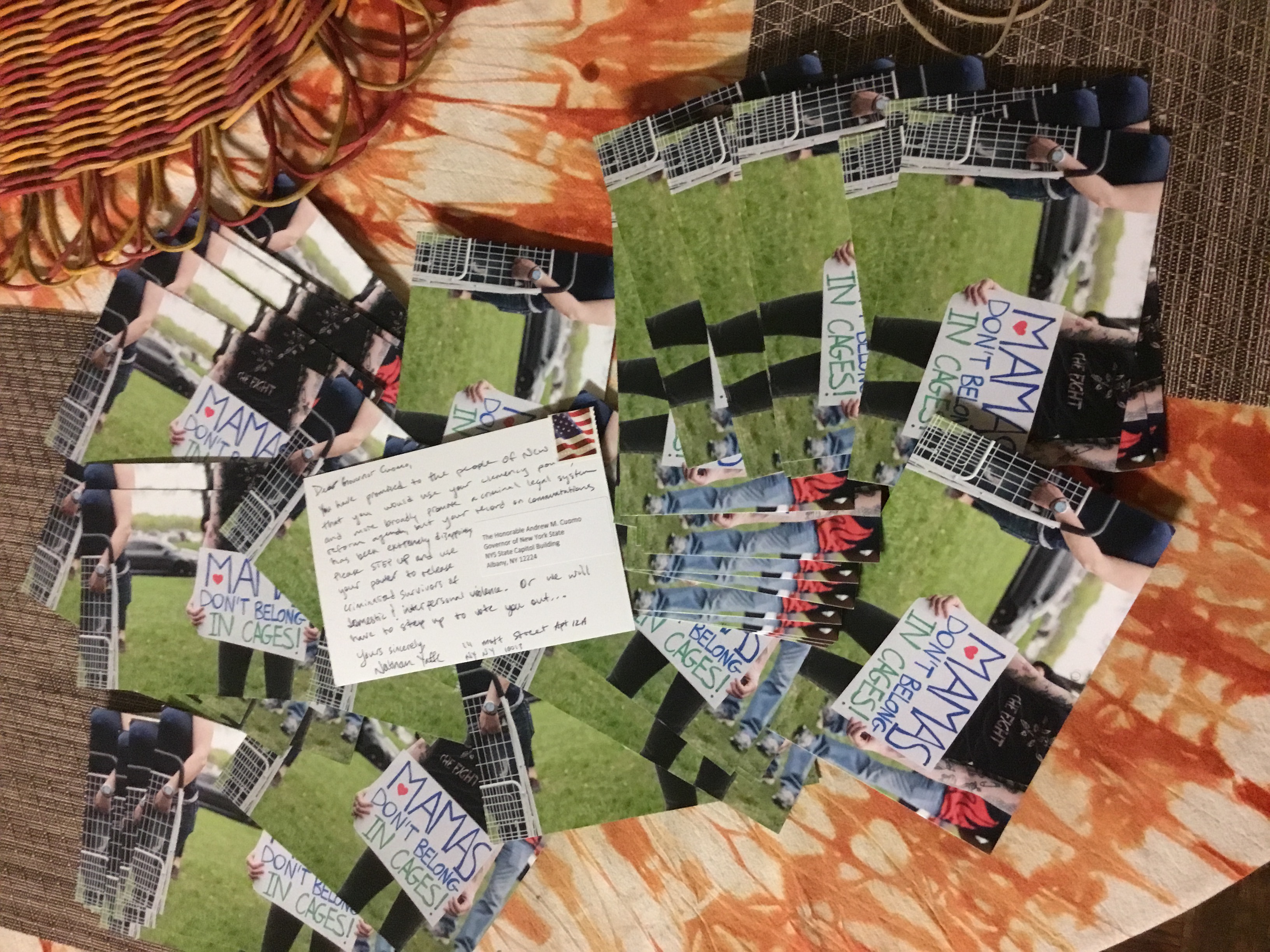 A picture of a large amount of survived and punished postcards in support of our campaign. Each postcard has art on the front including a person holding a sign saying: mamas don't belong in cages. One postcard is turned over to its back, with writing on it addressed to Governor Cuomo urging him to free survivors.